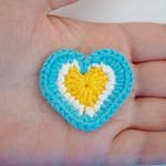 A colorful crochet heart rests on a hand, showcasing intricate handmade artistry.