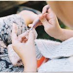 Woman crocheting outdoors, showcasing detail and texture in close focus. Perfect for craft and hobby themes.
